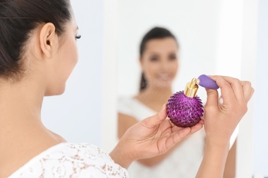 Photo of Young woman with bottle of perfume near mirror indoors