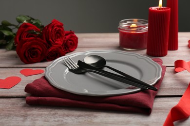Photo of Romantic place setting with red roses, candles and decorative hearts on wooden table. St. Valentine's day dinner