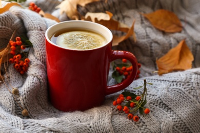 Photo of Cup of hot drink and autumn leaves on knitted sweater. Cozy atmosphere