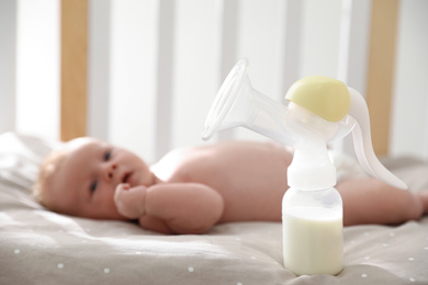 Photo of Healthy baby lying in cot, focus on breast pump with milk