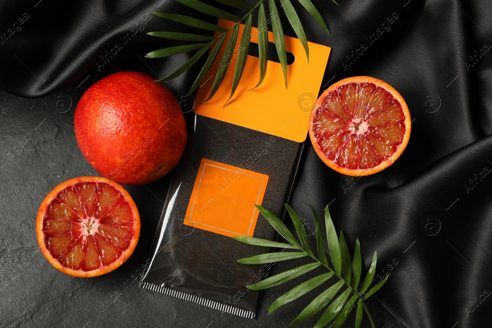 Photo of Scented sachet, red oranges and leaves on black table, flat lay