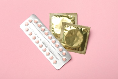 Condoms and birth control pills on pink background, top view. Safe sex