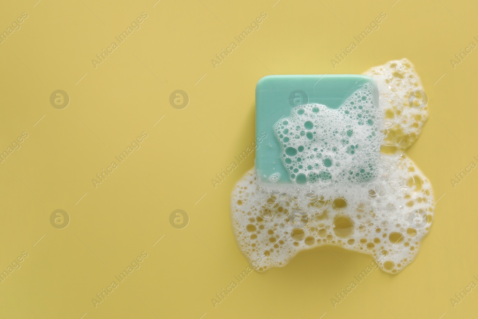Photo of Soap bar with fluffy foam on yellow background, top view. Space for text