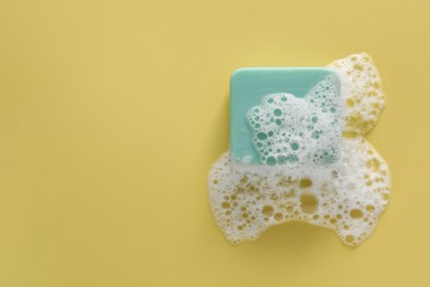 Soap bar with fluffy foam on yellow background, top view. Space for text