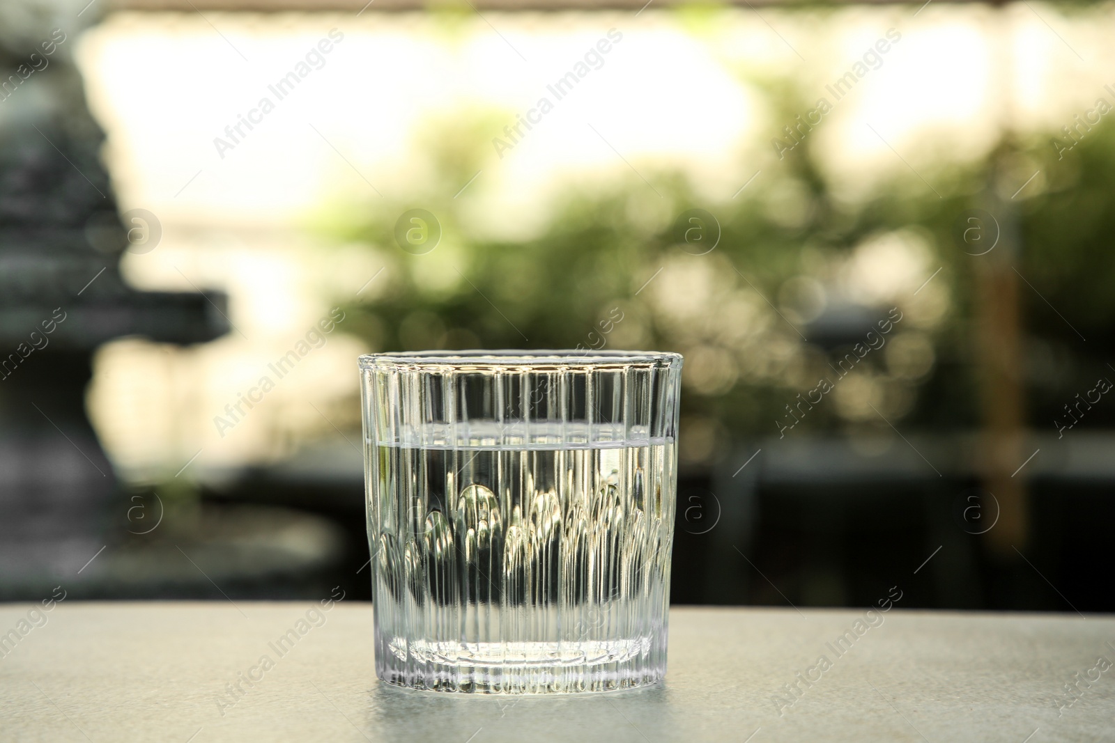 Photo of Glass of fresh water on light grey table outdoors