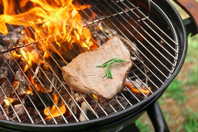 Photo of Tasty meat on barbecue grill with fire flames outdoors, closeup