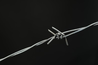 Shiny metal barbed wire on dark grey background, closeup