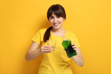 Young woman using mouthwash on yellow background