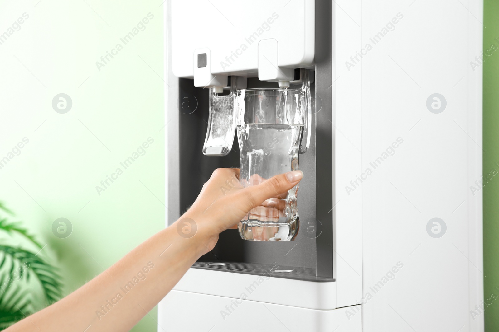 Photo of Woman filling glass from water cooler indoors, closeup. Refreshing drink