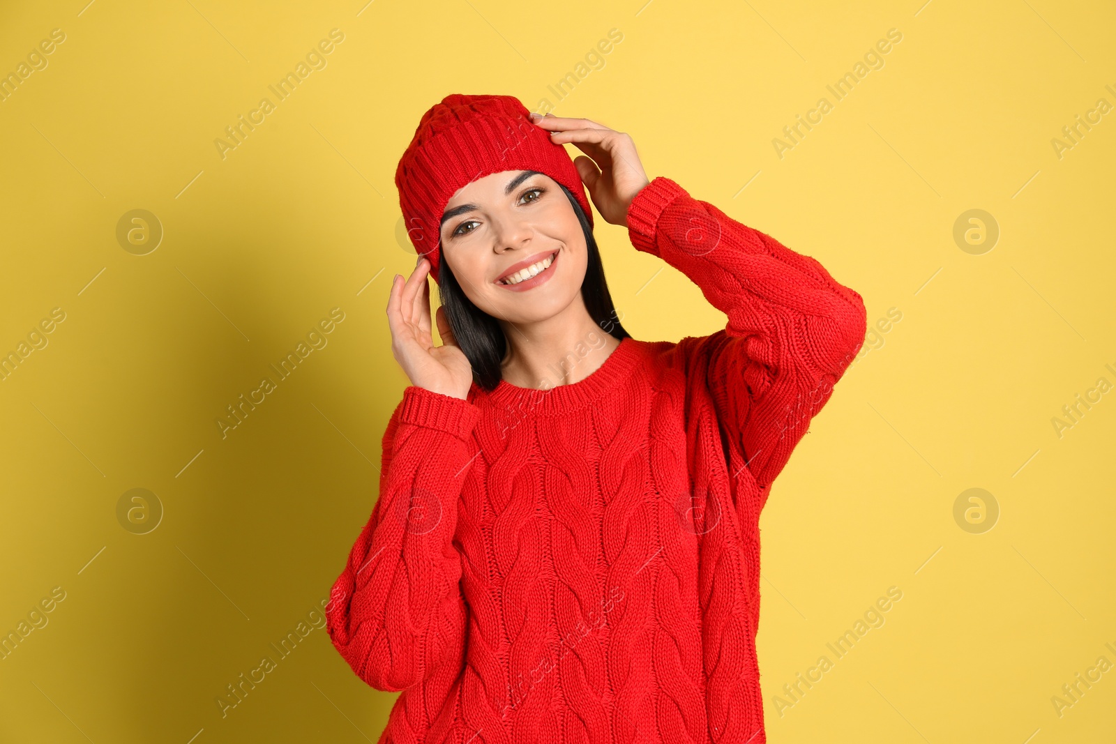 Photo of Young woman wearing warm sweater and hat on yellow background. Winter season