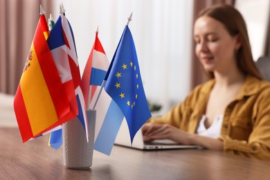 Photo of Woman working with laptop at table indoors, focus on different flags