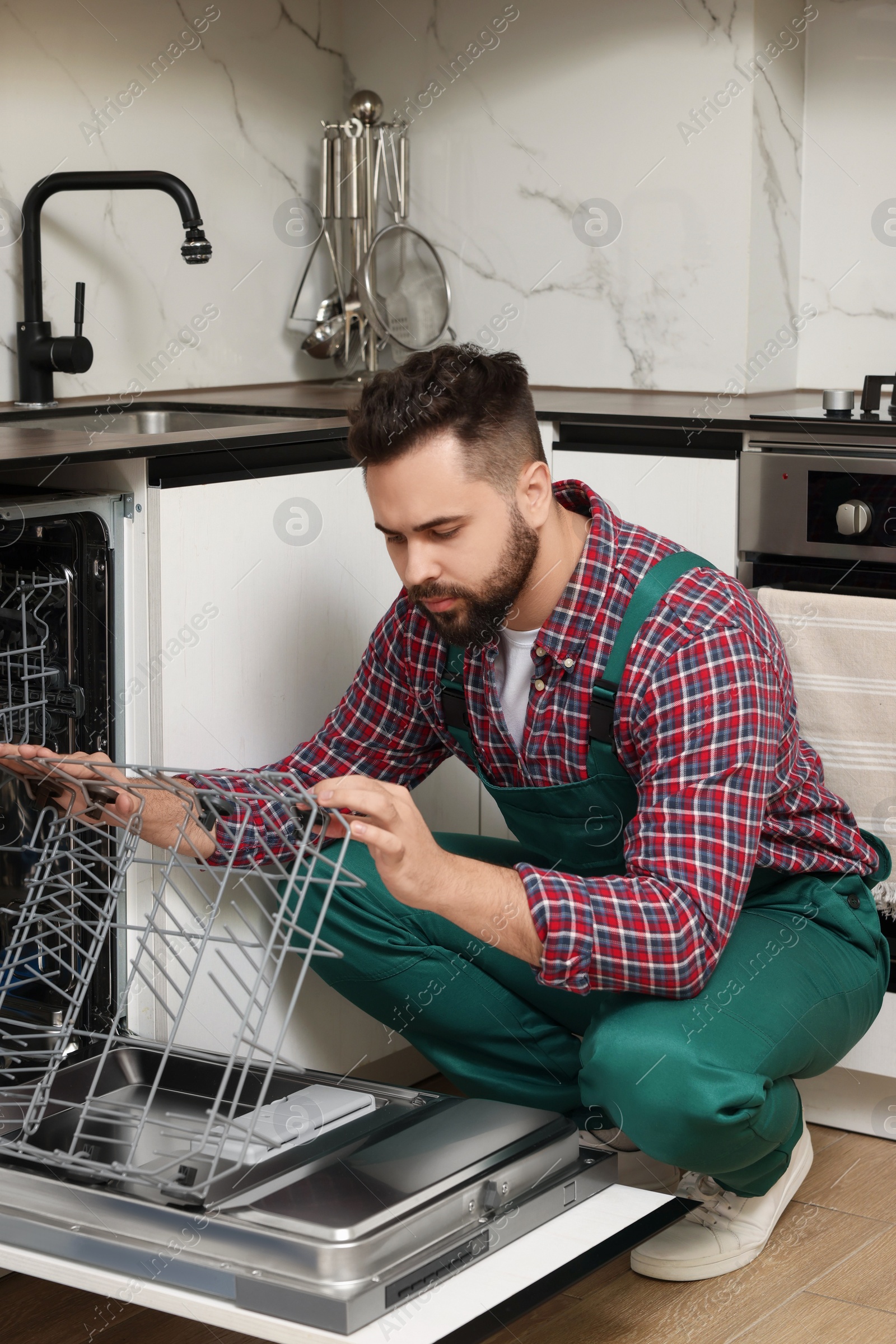 Photo of Serviceman examining dishwasher lower rack in kitchen