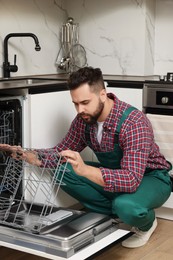 Serviceman examining dishwasher lower rack in kitchen