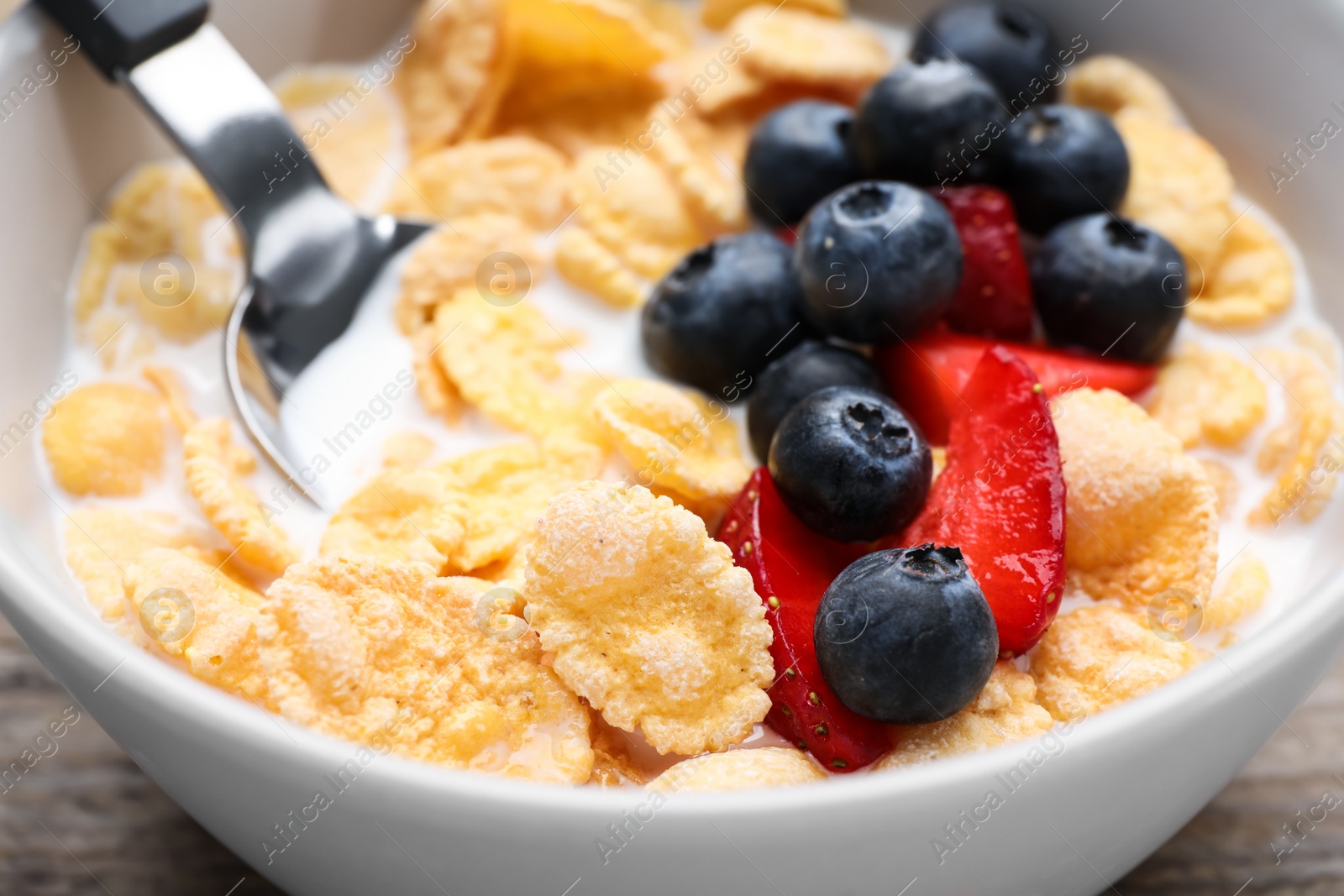 Photo of Bowl of tasty crispy corn flakes with milk and berries on wooden table, closeup