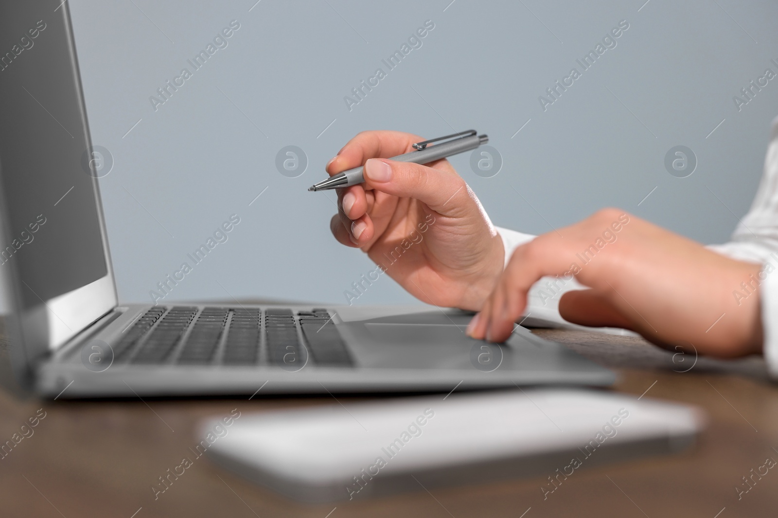 Photo of Woman with smartphone and pen working on laptop at wooden table, closeup. Electronic document management