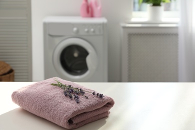 Photo of Folded clean towel and lavender flowers on white table indoors. Space for text