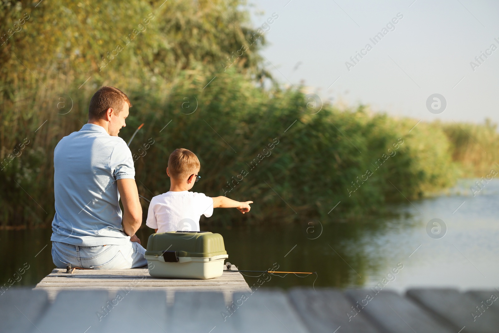 Photo of Dad and son fishing together on sunny day. Space for text