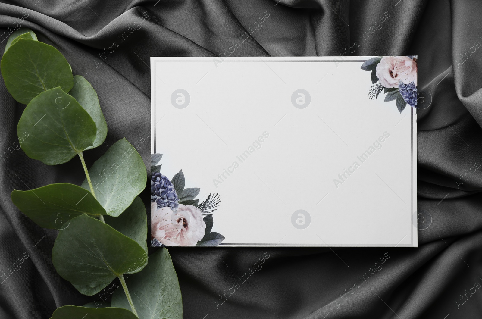 Photo of Blank invitation card and eucalyptus leaves on black fabric, flat lay