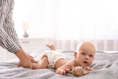 Young woman massaging cute little baby on bed at home