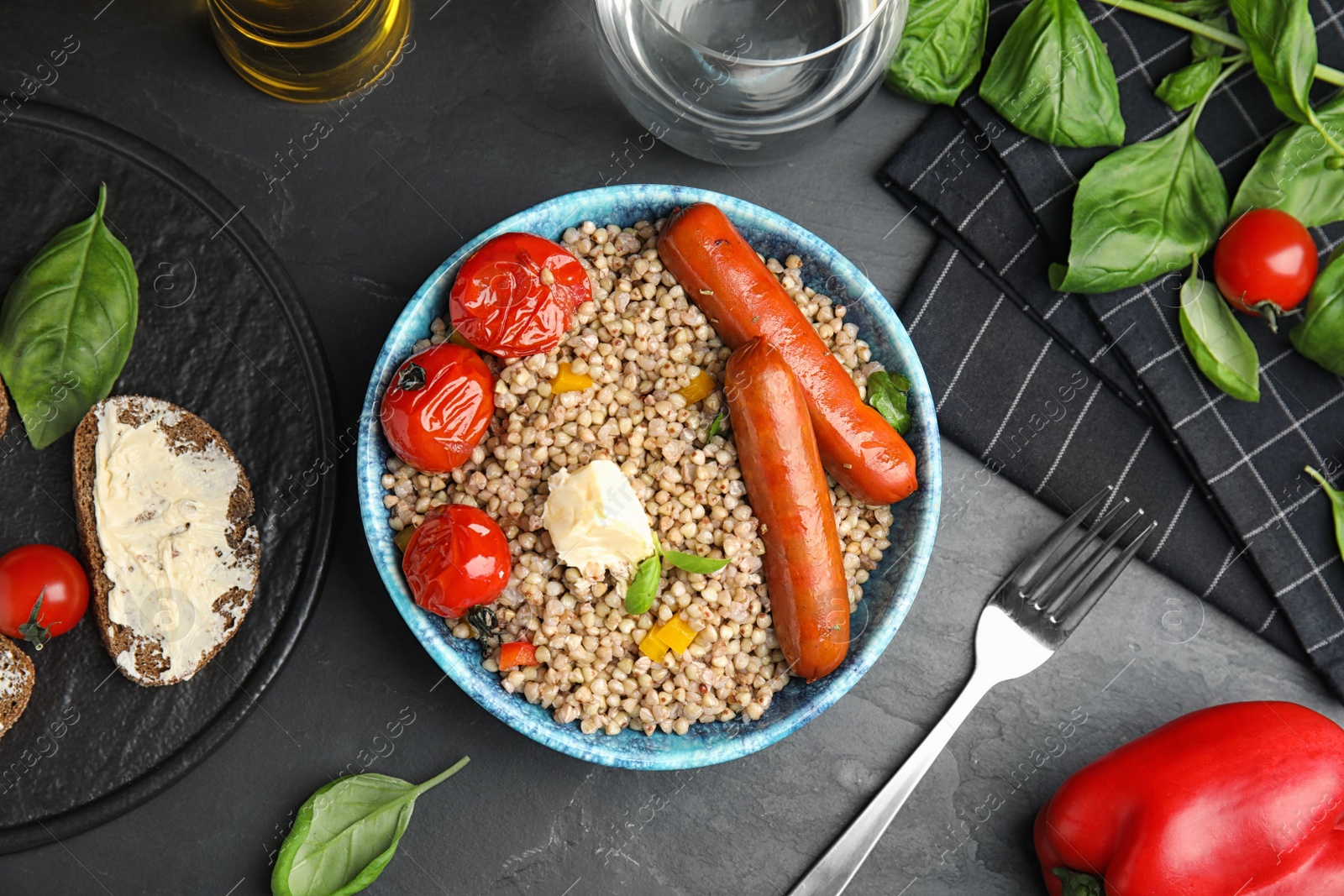 Photo of Tasty buckwheat porridge with sausages on dark grey table, flat lay