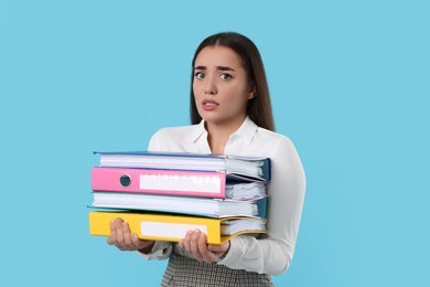 Stressful woman with folders on light blue background