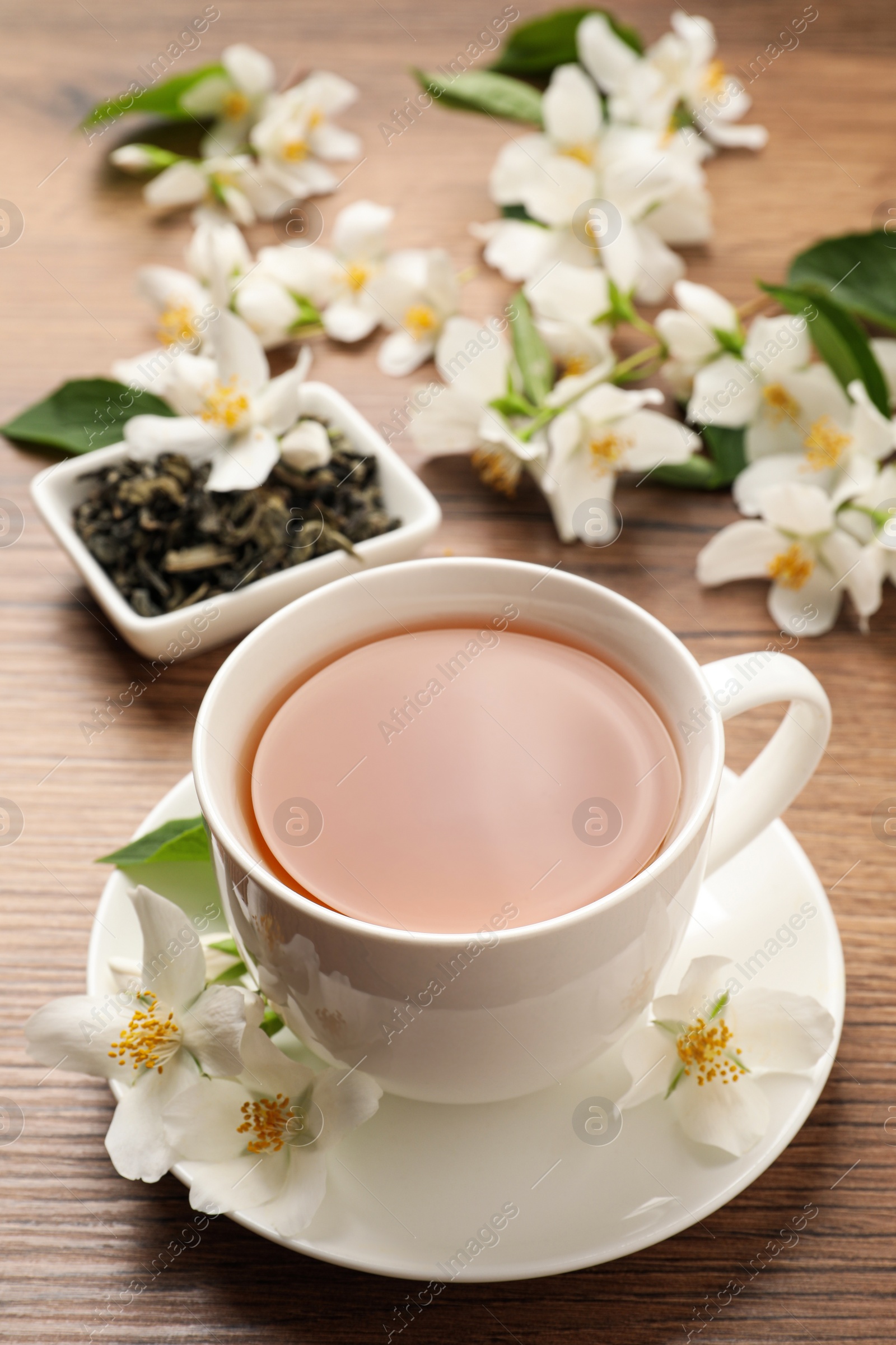 Photo of Cup of aromatic jasmine tea and fresh flowers on wooden table