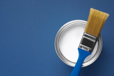 Photo of Can with white paint and brush on blue background, top view. Space for text