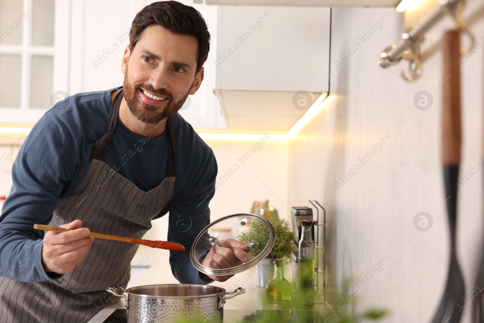 Photo of Man cooking tomato soup on cooktop in kitchen