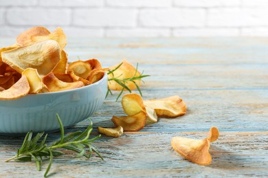 Photo of Bowl of tasty homemade parsnip chips and rosemary on old light blue wooden table. Space for text