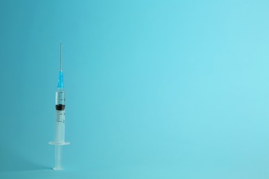 Photo of Medical syringe with liquid on light blue background, space for text