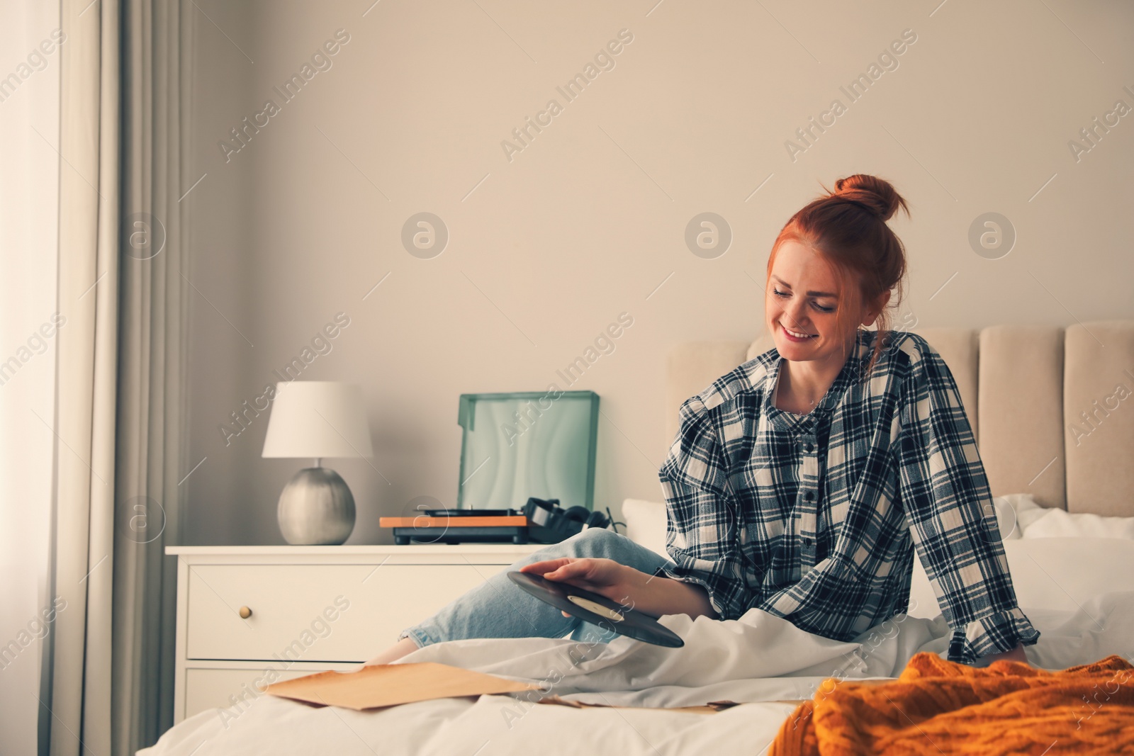 Photo of Young woman choosing vinyl disc to play music with turntable in bedroom