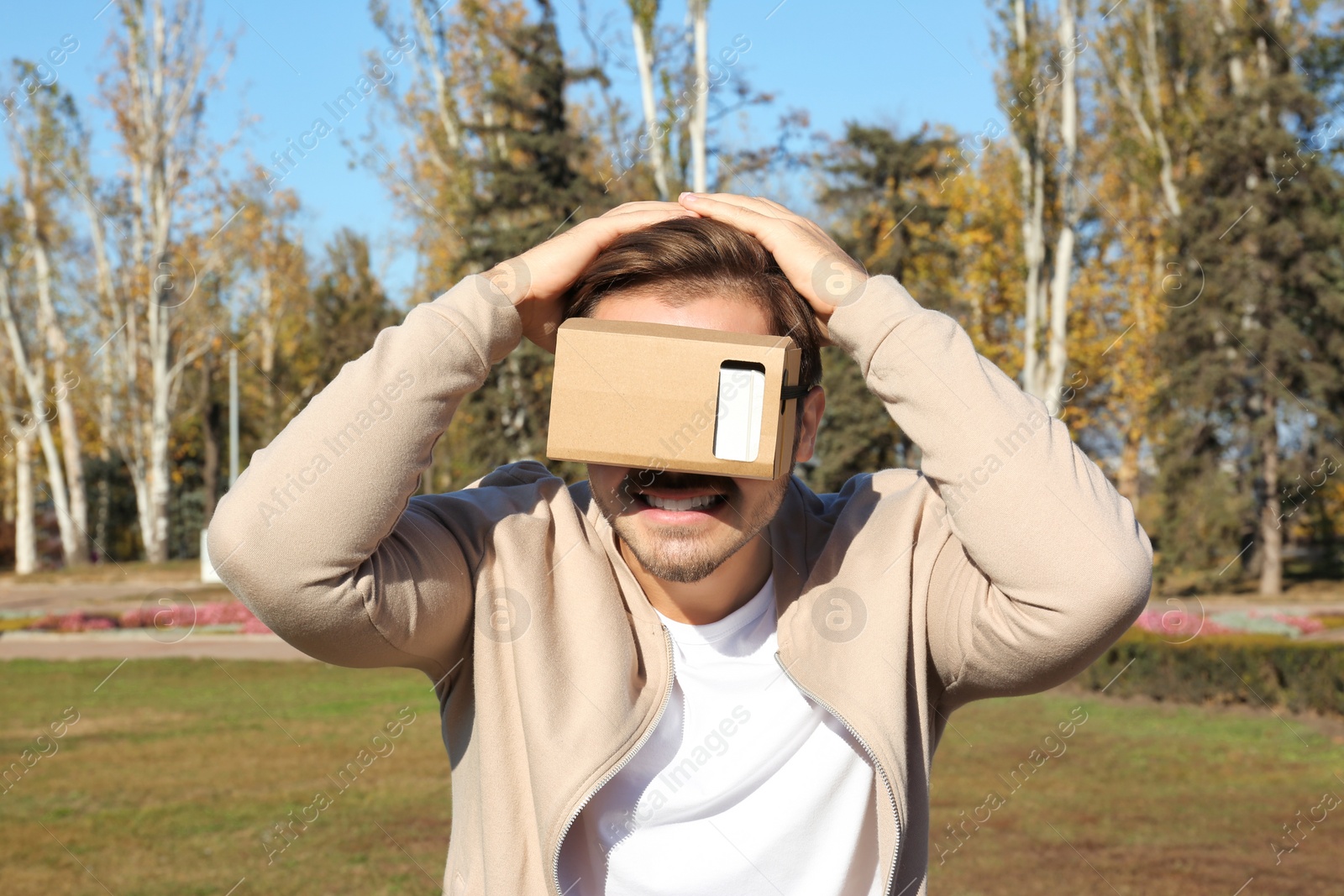 Photo of Young man using cardboard virtual reality headset outdoors