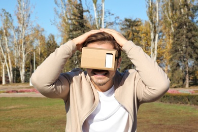 Young man using cardboard virtual reality headset outdoors