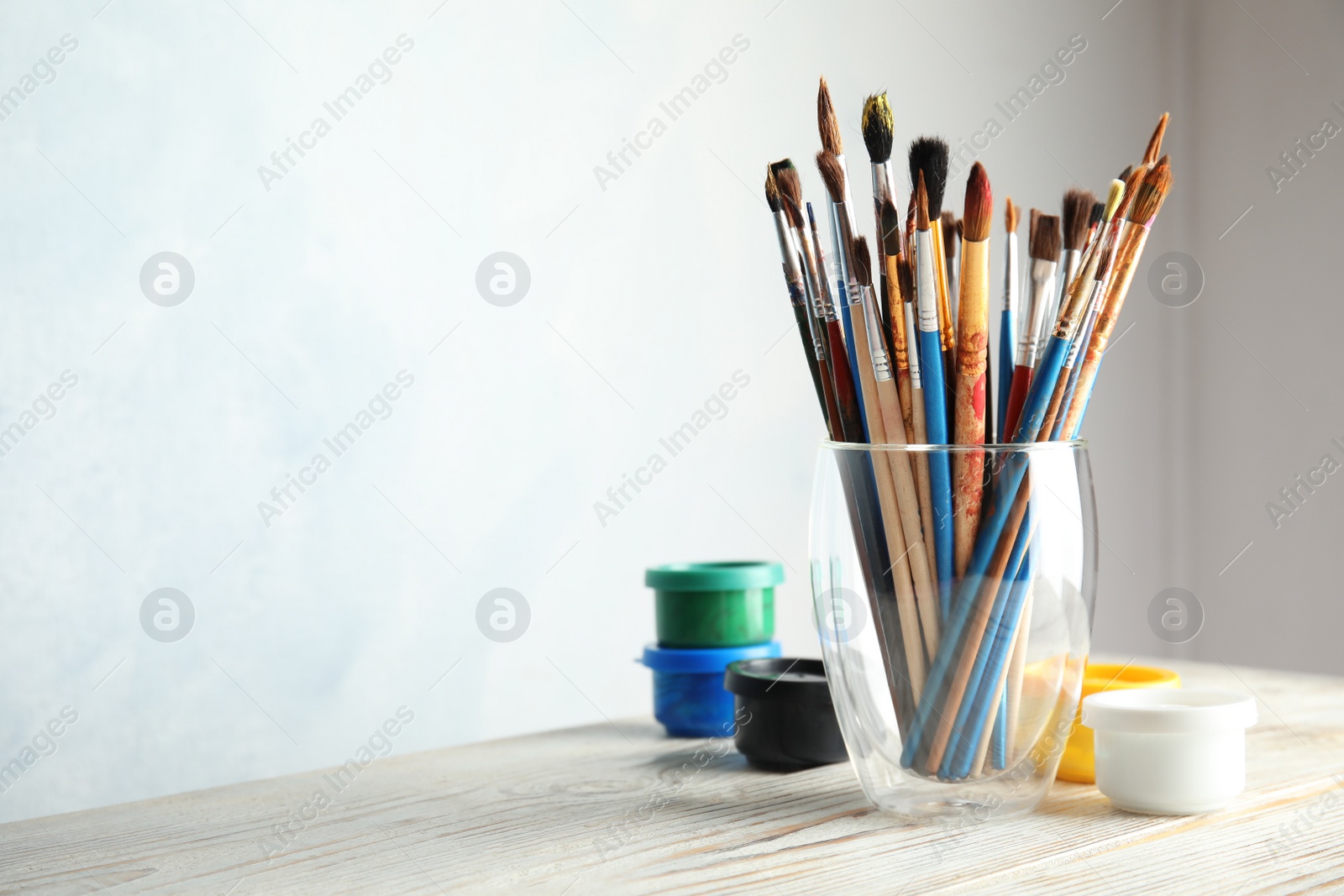 Photo of Glass with brushes and paint jars on table against light background. Space for text