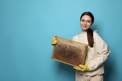Photo of Beekeeper in uniform holding hive frame with honeycomb on light blue background. Space for text