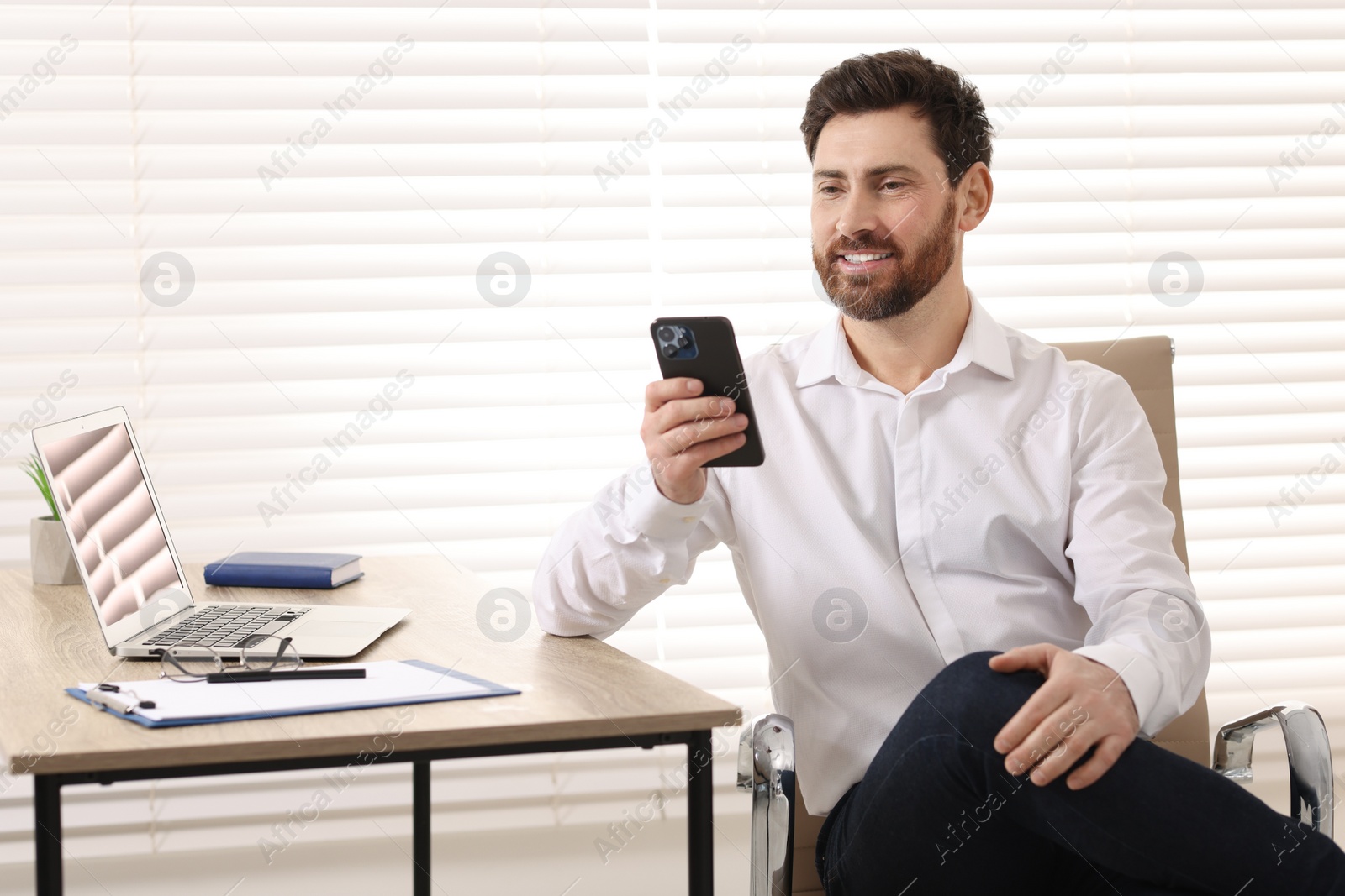 Photo of Smiling man using smartphone at table in office