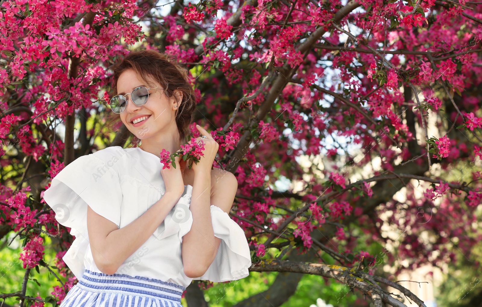 Photo of Attractive young woman posing near blossoming tree on sunny spring day