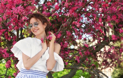 Attractive young woman posing near blossoming tree on sunny spring day