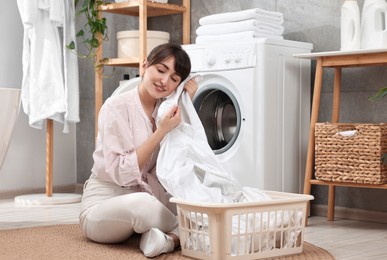 Photo of Young housewife with laundry near washing machine at home