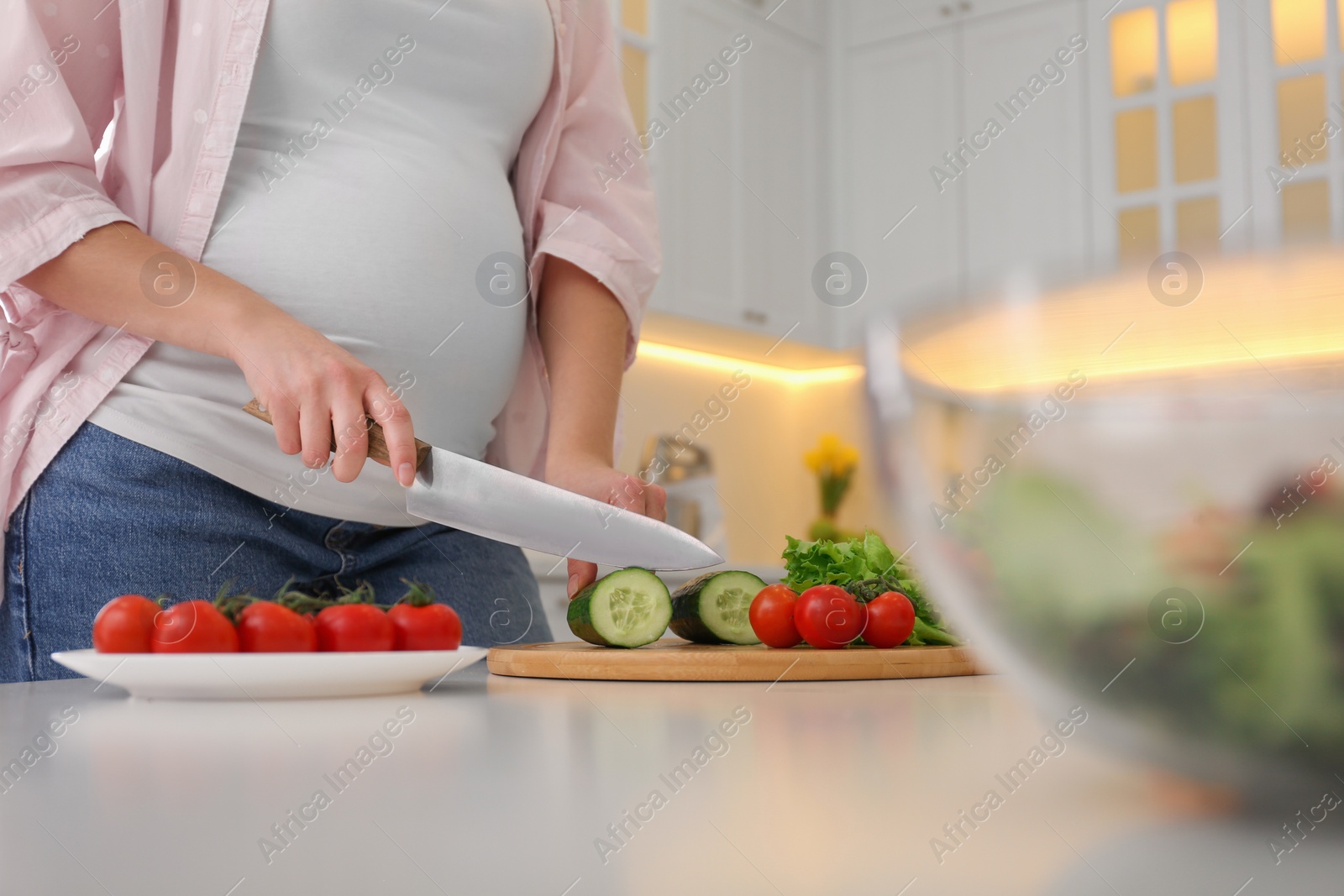 Photo of Young pregnant woman preparing vegetable salad at table in kitchen, closeup. Healthy eating