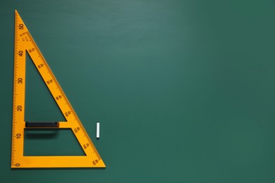 Photo of Yellow triangle and chalk on green chalkboard, flat lay. Space for text