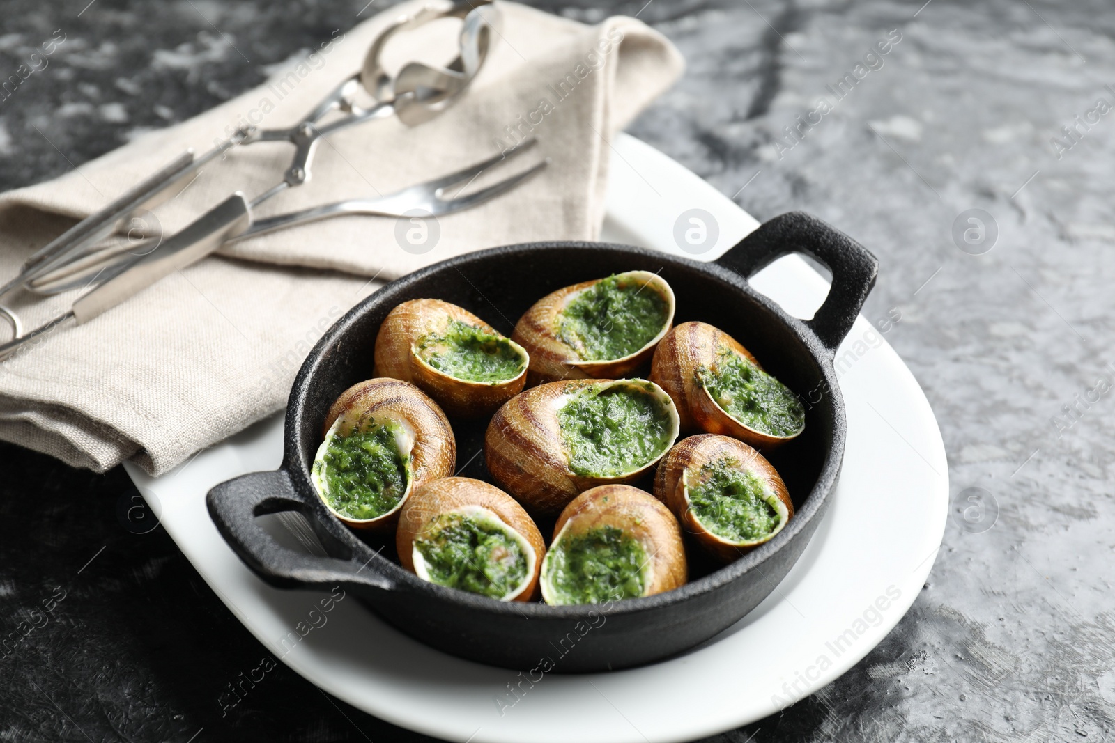 Photo of Delicious cooked snails in baking dish served on grey textured table