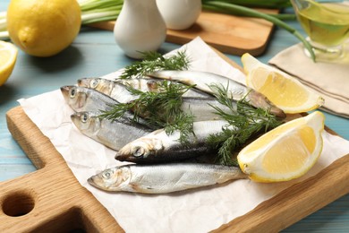 Photo of Fresh raw sprats, dill and cut lemon on light blue wooden table, closeup