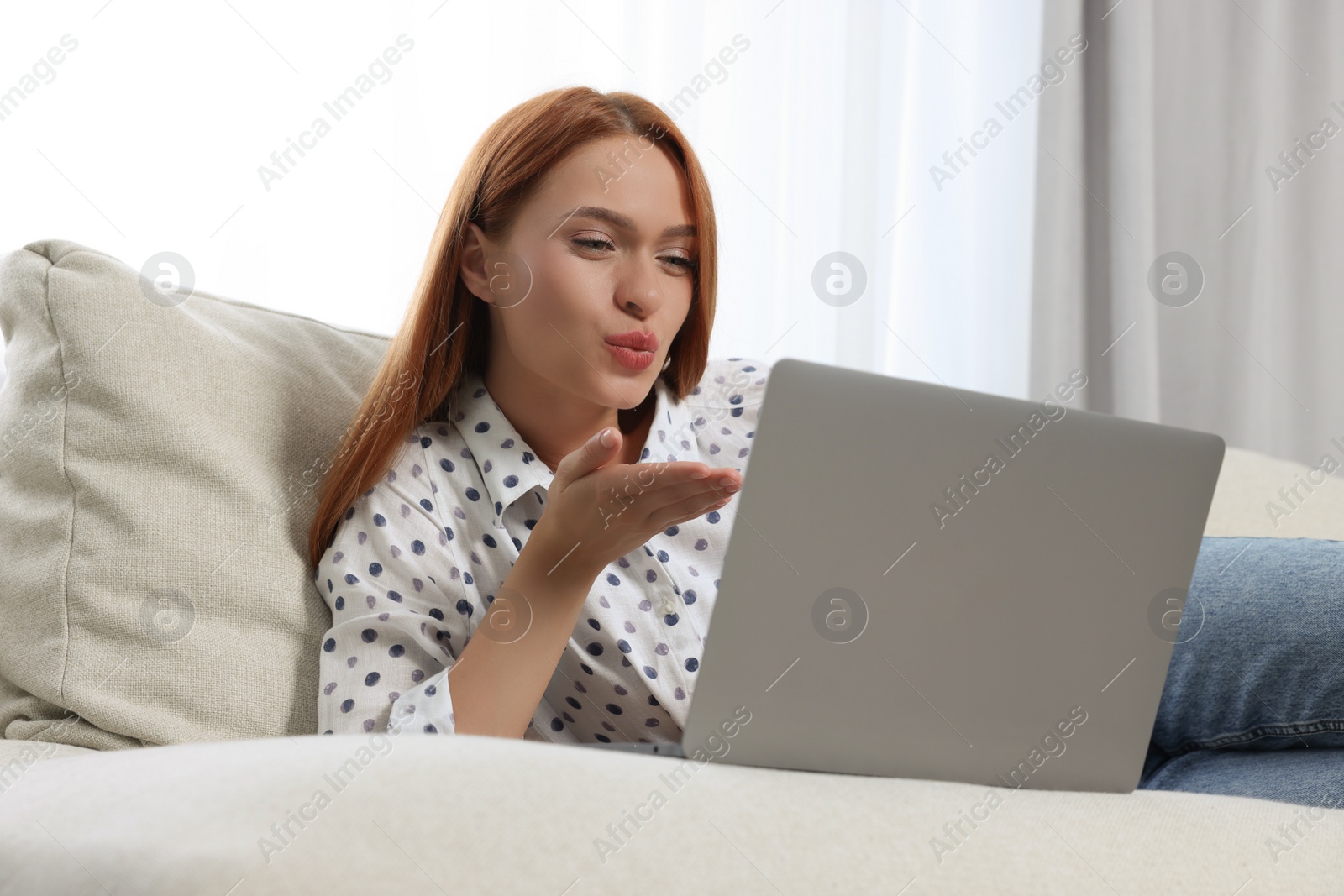 Photo of Woman blowing kiss during video chat via laptop at home. Long-distance relationship