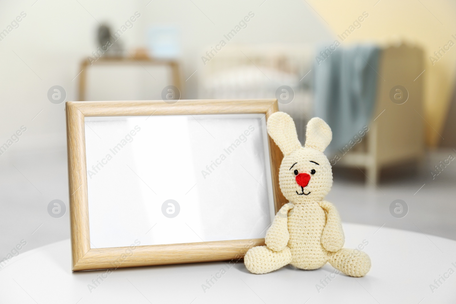 Photo of Photo frame and toy bunny on table in baby room interior. Space for text