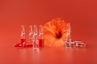 Skincare ampoules and hibiscus flower on coral background