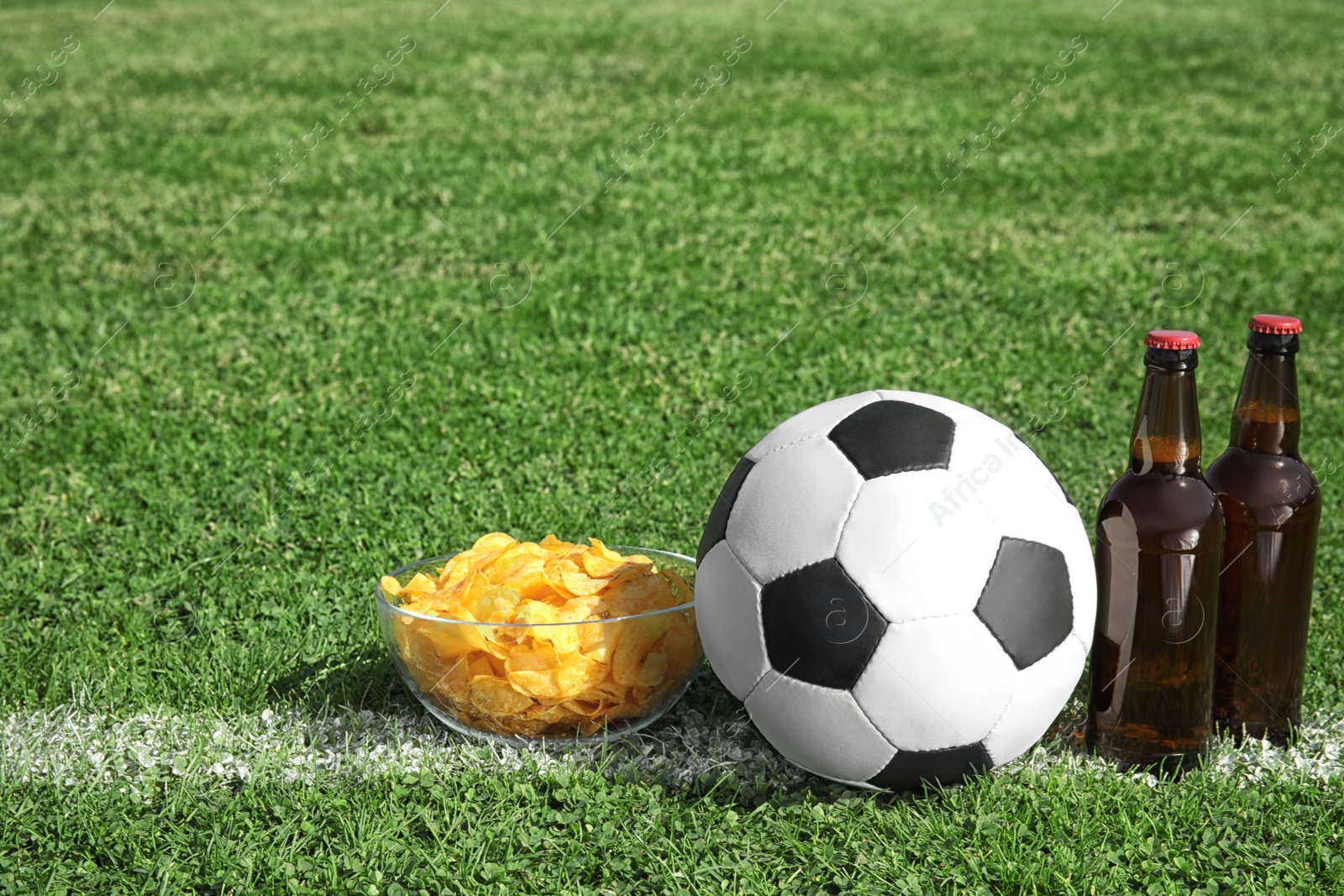 Photo of Soccer ball with beverage and chips on green football field grass. Space for text