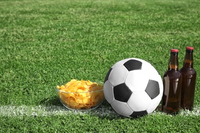 Photo of Soccer ball with beverage and chips on green football field grass. Space for text