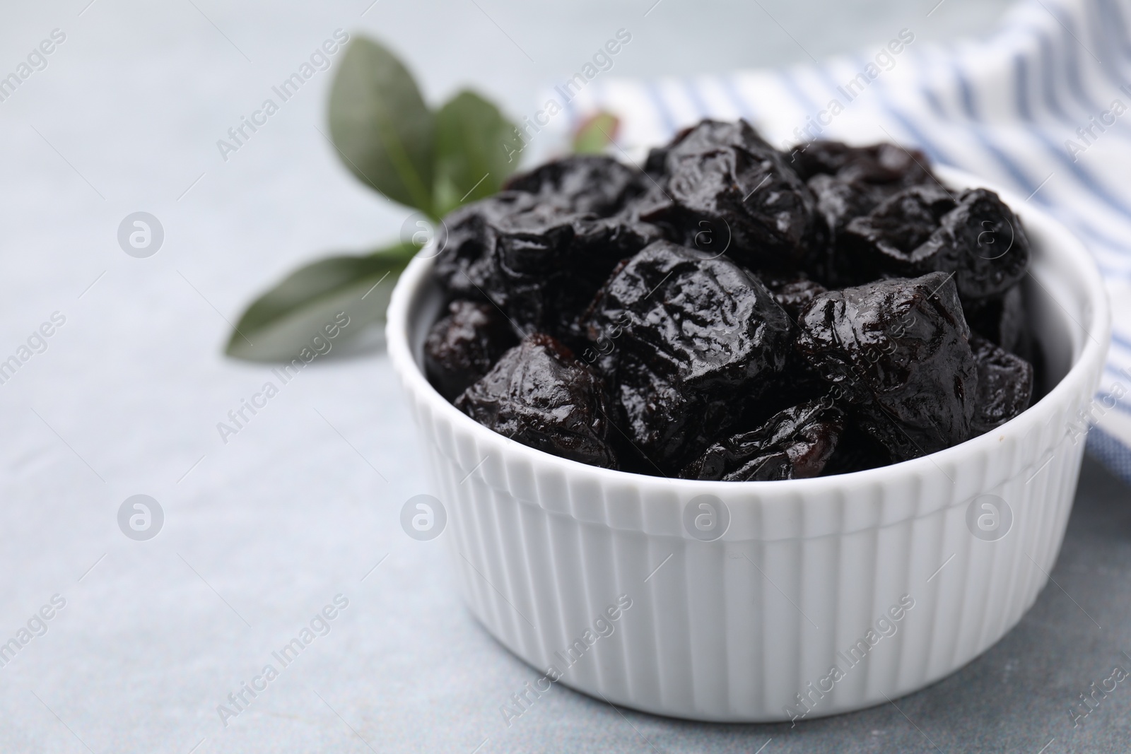 Photo of Sweet dried prunes in bowl on light grey table, closeup. Space for text