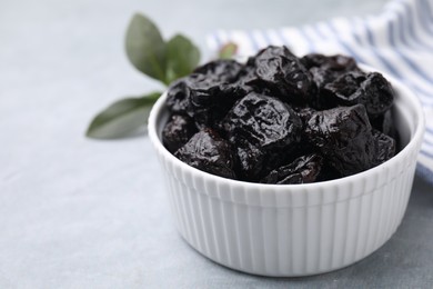 Sweet dried prunes in bowl on light grey table, closeup. Space for text